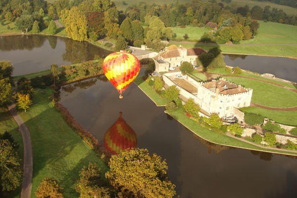 Hot air balloon flying over water and two large white houses in the sun