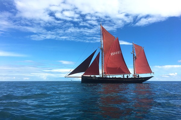 Sailing boat with big red sails sailing over a calm sea under beautiful blue skies