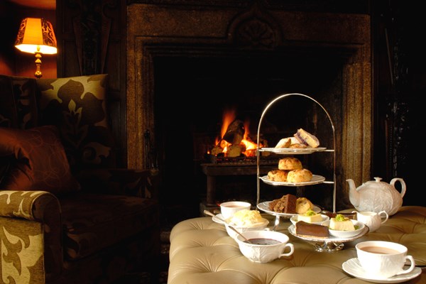 Delicious selection of afternoon tea treats and pots of tea next to an open fire