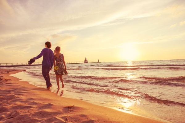 Two people holding hands walking along a sandy beach in Cornwall